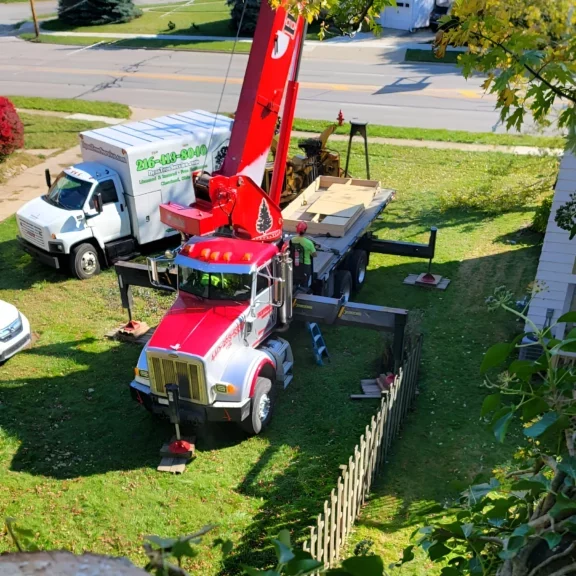 A large red and white crane truck parked on a residential lawn, preparing for tree removal, with another company truck nearby.